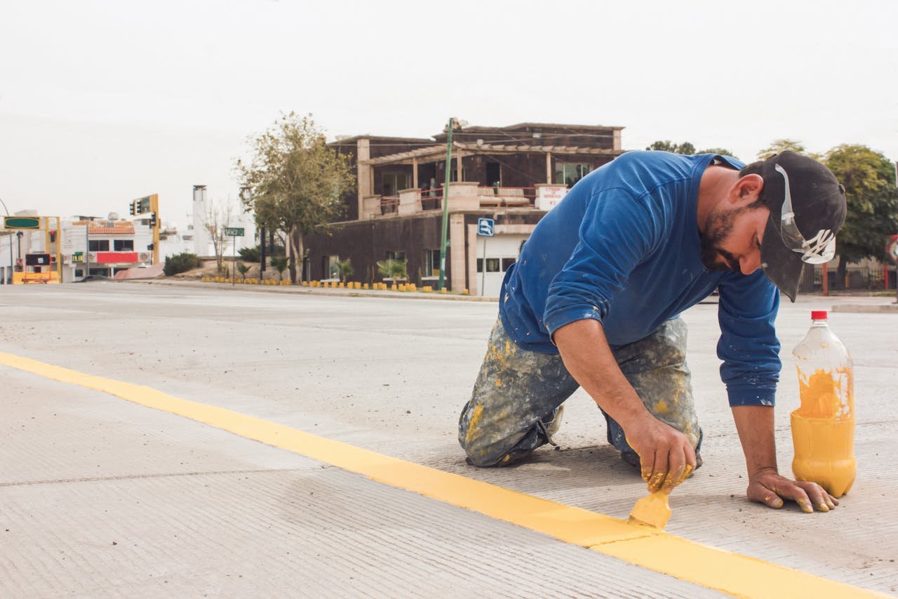 services-05 A man paints yellow road lines on an urban street, emphasizing urban infrastructure and maintenance.